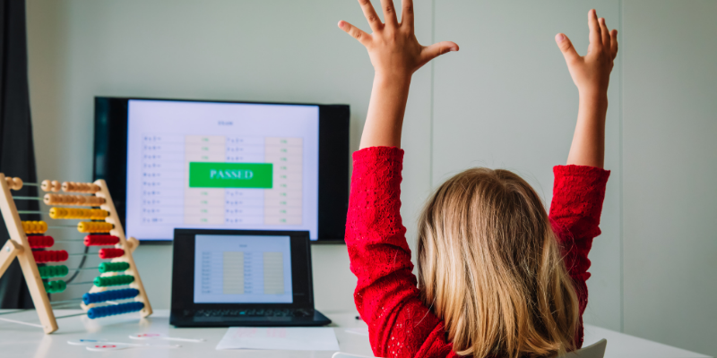 A girl raises her hands in celebration as she looks at her computer where it shows she has passed a test as a visual representation of momentum for students
