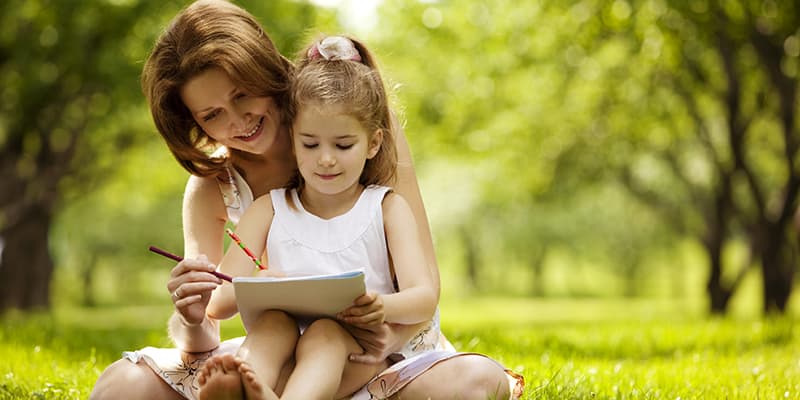 Mother reading to daughter on her lap outside