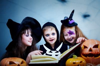 three kids in Halloween costumes reading a spooky story