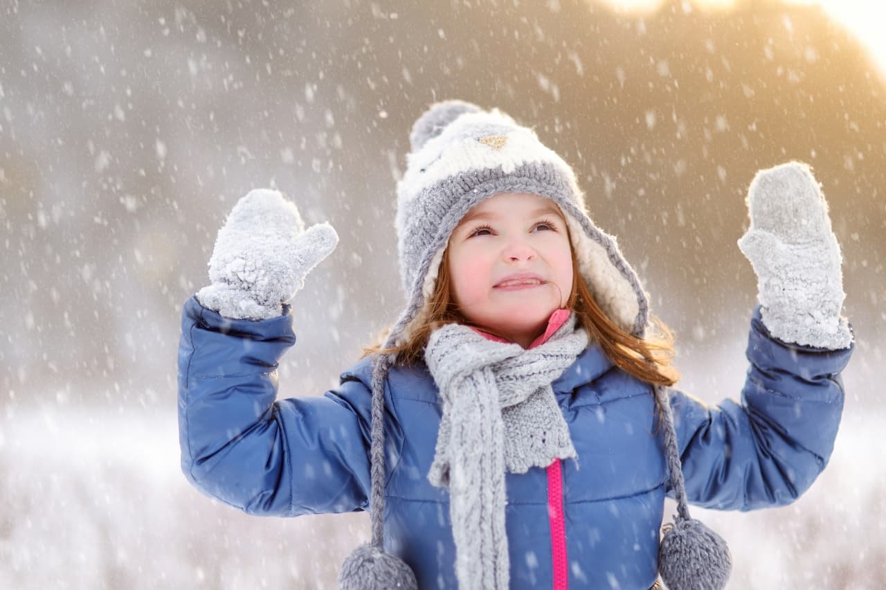a young girl outside with her hands raised towards the falling snow