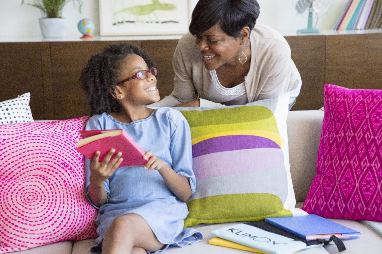 mother leaning over to talk to her daughter while she is sitting on the couch studying