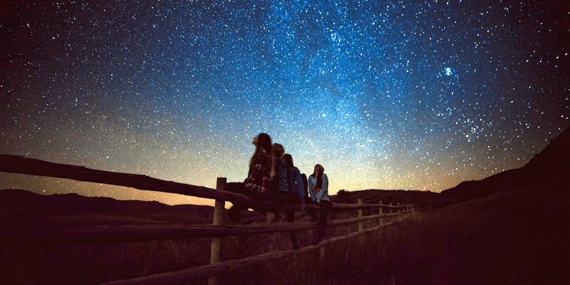 Girls sitting on a fence stargazing after parents look into how to teach constellations.