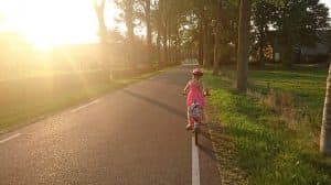 Child riding a bicycle with the sun shining on her.