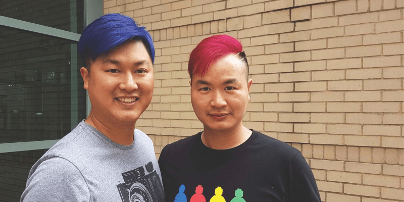 Jason and Rico stand in front of a brick wall with their blue and red hair