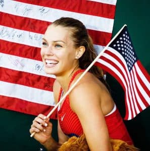 Colleen grins holding an American flag standing in front of another American flag.
