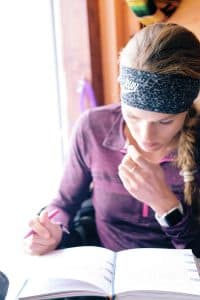 Colleen writes in her journal wearing a maroon top and a large headband
