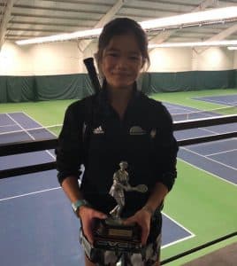 Hazel poses on a tennis court with her racket and a trophy