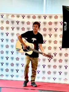Joshua plays guitar in front of a step and repeat