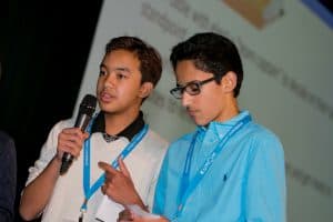 Joshua stands with a microphone next to another student at the student conference