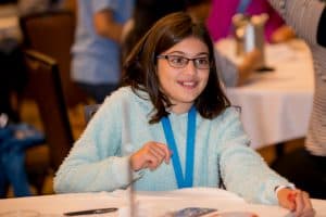 Cara sits at a table wearing a blue shirt at the Student Conference
