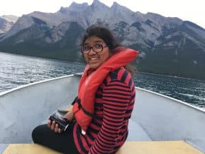 Zainab sits in a boat with a life vest on with mountains in the background