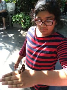 Zainab stands in a red and blue striped shirt with a butterfly on her hand