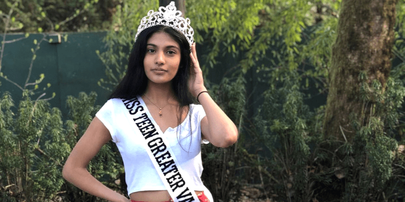 Khushi stands in a white shirt and sash with her crown