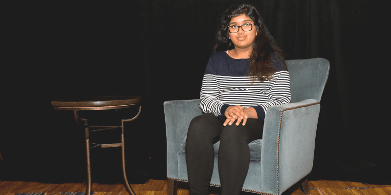 Zainab poses in a blue chair wearing a black and white striped shirt at the student conference