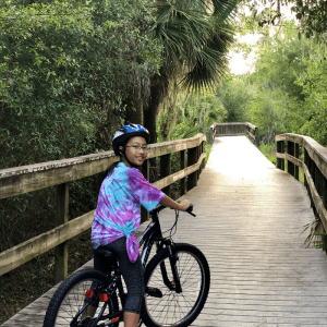 Anna rides her bike down a tree-lined path