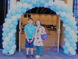 Ravi stands with his Instructor in front of a blue and white balloon arch.