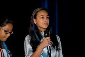 Keya speaks into a microphone at the student conference