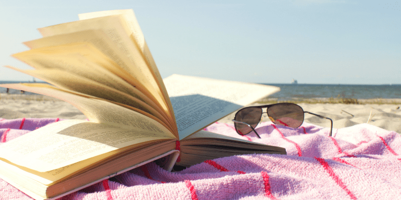 A book and sunglasses sits on a towel at the beach ready