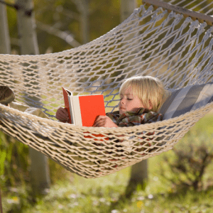 a young boy reads a book in a hammock