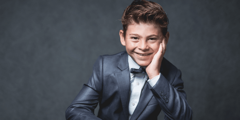 Connor poses against a gray background wearing a tuxedo