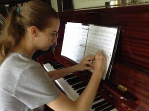 Sophia makes a notation in her sheet music while sitting at the piano