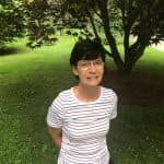 Laura stands in a striped shirt in front of a tree