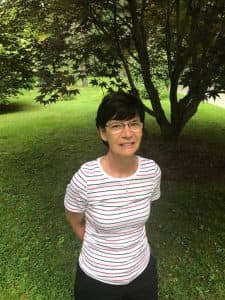 Laura stands in a striped shirt in front of a tree