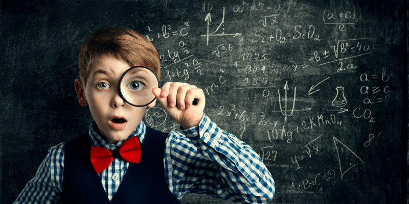 Boy stands in front of blackboard with a magnifying glass