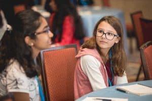 Zosia looks at another student while seated at a table during the Student Conference
