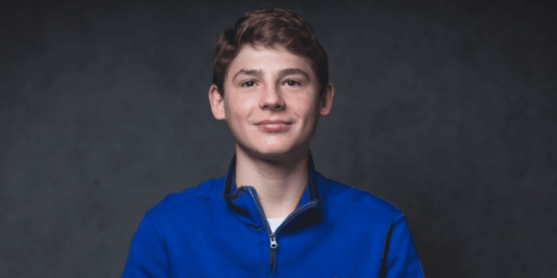 Aidan poses in a blue fleece in front of a grey background