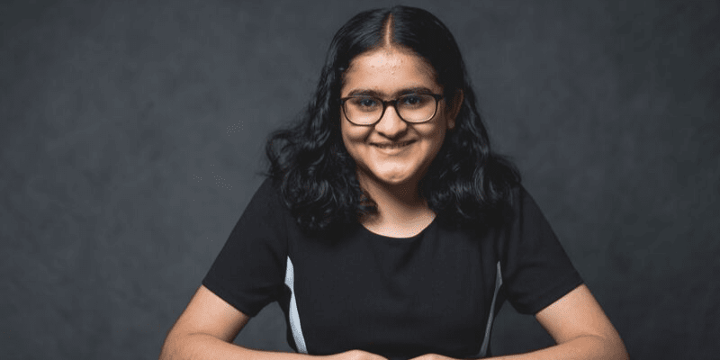 Vidhi sits in front of a gray background wearing a black dress