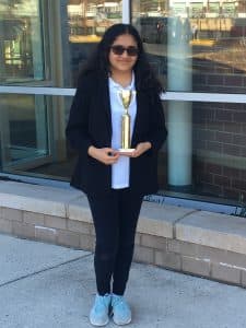 Vidhi stands outside a building holding a trophy