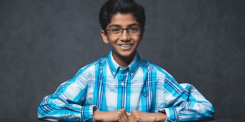 Shaylen poses in front of a gray background wearing a blue plaid shirt