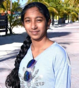 Rishika poses in front of palm trees with a blue shirt and braid