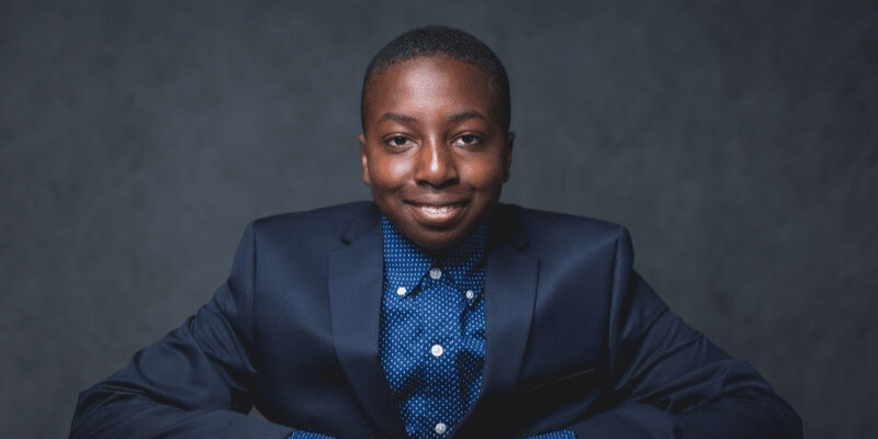 Temi poses in a navy suit in front of a gray background at the student conference