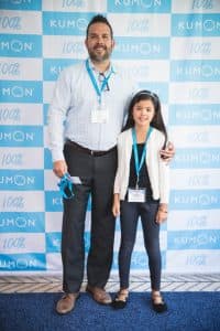 Jessica poses with her dad in front of a Kumon backdrop