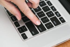 a hand presses the "enter" button on a Macbook keyboard