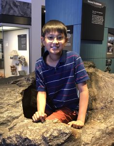 student in striped shirt and glasses is sitting on a brown cave-like sculpture