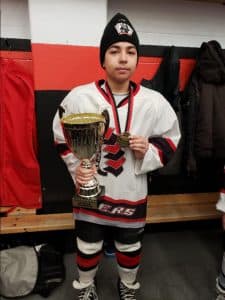 Hargoun poses with a trophy wearing his hockey uniform in a locker room