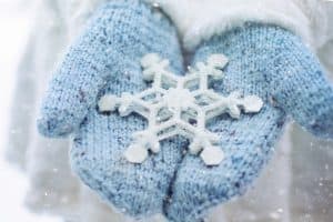 A large snowflake is held in two outstretched hands wearing blue mittens