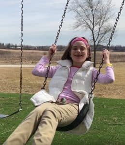 young girl at the park with hands on the swing set