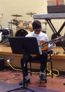 student playing guitar in a school auditorium 