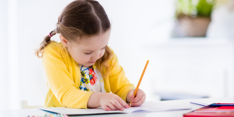 Young girl wearing a yellow cardigan and properly holding a pencil working on homework