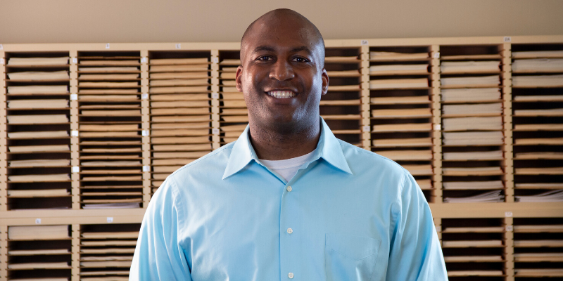 Kumon Instructor standing in front of worksheet cubbies wearing a blue button up.