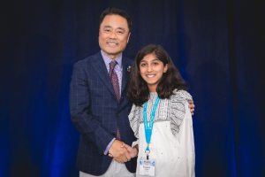 Kumon Instructor shakes the hand of his student on stage in front of blue curtain