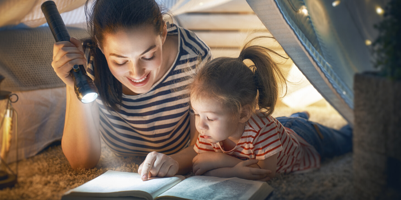 Mom and Daughter Reading a Book indoors with a flashlight