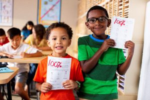 two students holding up their 100% accomplishment on a recent worksheet
