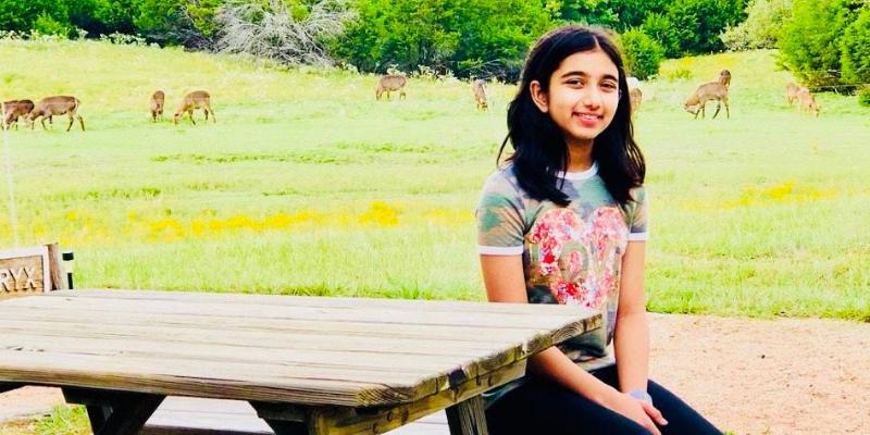 portrait photo of a student sitting at a picnic table with a field full of animals in the background