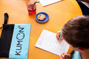 Student working on Kumon Worksheets with pouch on the left and juice and cookie on the right