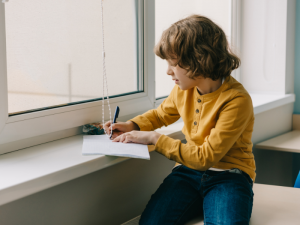 young boy does his homework on a window sill